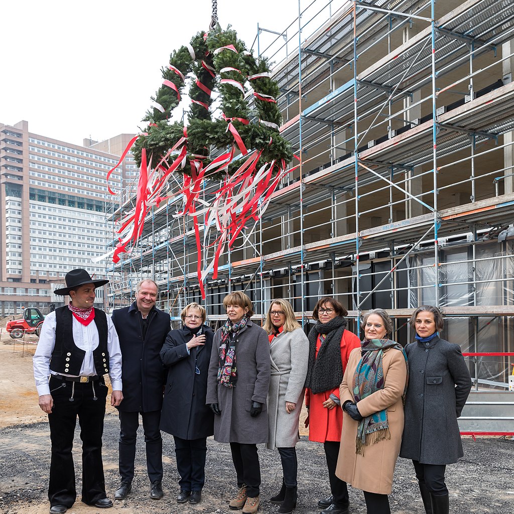 Gruppenfoto mit traditionell gekleidetem Handwerker, darüber ein Richtkranz, dahinter Rohbau mit Gerüst